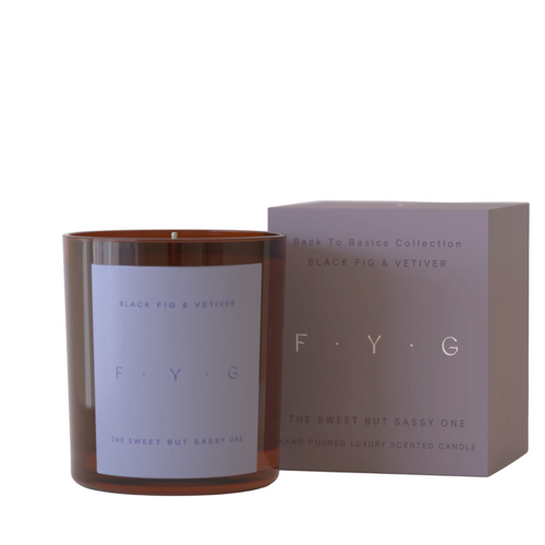 An amber glass scented candle with a lavender label next to its matching mauve-colored packaging box, both featuring the brand name F.Y.