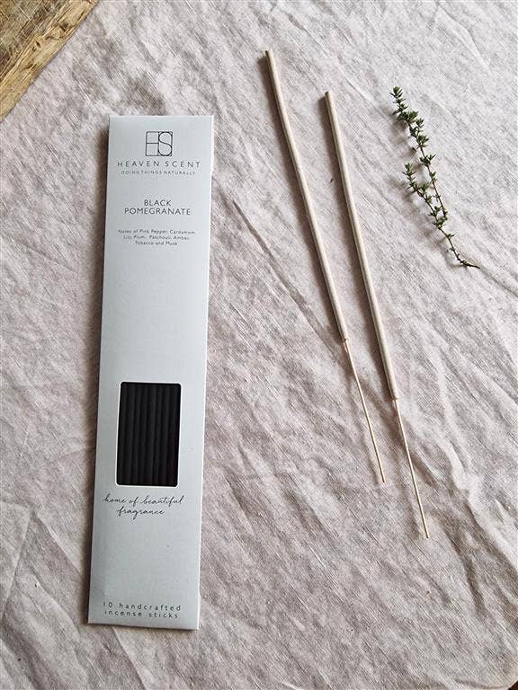 Heaven Scent Black Pomegranate essential oil diffuser wicks shown next to their white packaging box on a textured beige linen fabric background, styled with a sprig of green herbs.