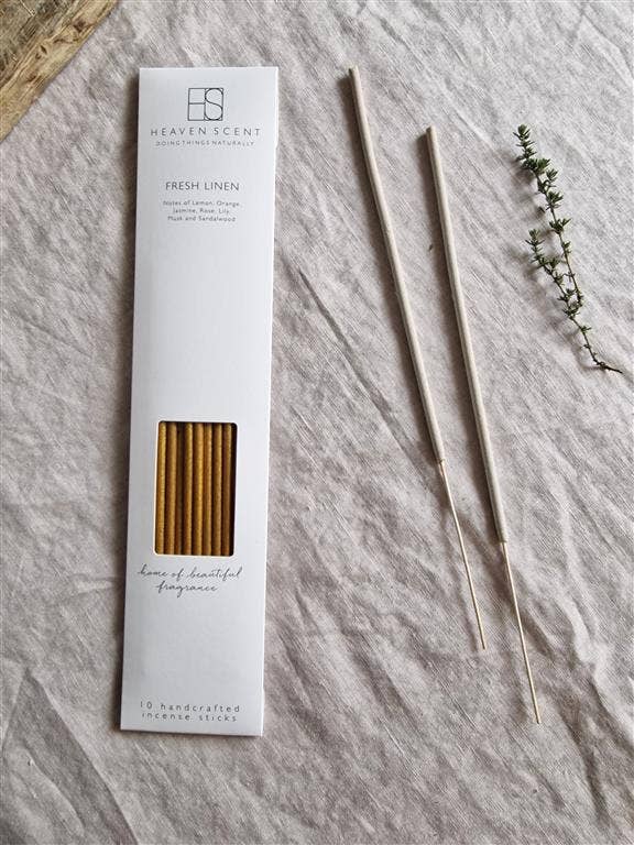 Heaven Scent Fresh Linen handcrafted incense sticks in a white box, displayed next to two unbaked incense sticks on a textured light gray linen fabric background with dried botanical props.