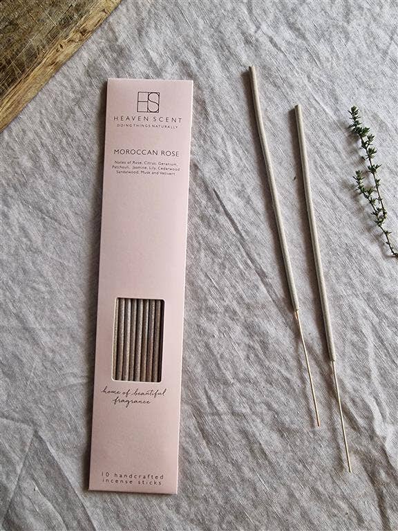 Heaven Scent Moroccan Rose incense sticks shown with their pale pink packaging box and two loose incense sticks on a textured light gray fabric background.
