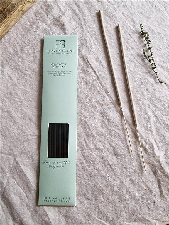 Heaven Scent 'Oakwood & Cedar' 10-handcrafted scented sticks in a light mint green box, displayed on a textured light gray linen fabric alongside two wooden sticks and a small sprig of greenery.