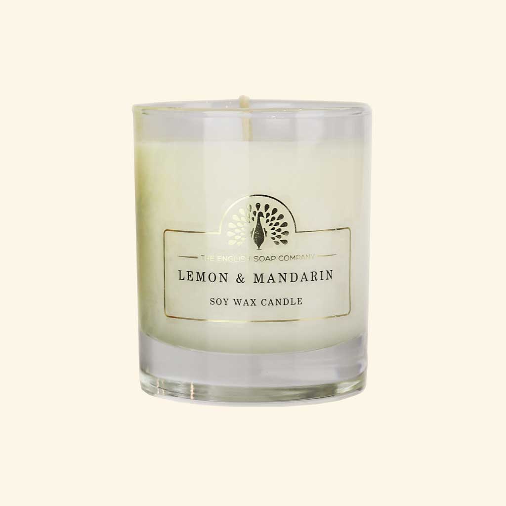 A soy wax candle in a clear glass jar with a white label reading 'The Smokey Soap Company Lemon & Mandarin Soy Wax Candle' on a light cream background.