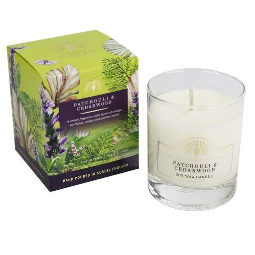 Patchouli & Cedarwood soy wax candle in a clear glass jar next to its green and purple illustrated packaging box on a white background. - The Fig House