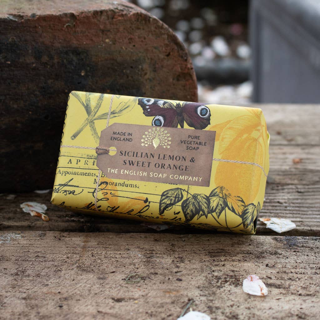Bar of soap with yellow packaging featuring botanical designs on a wooden surface.