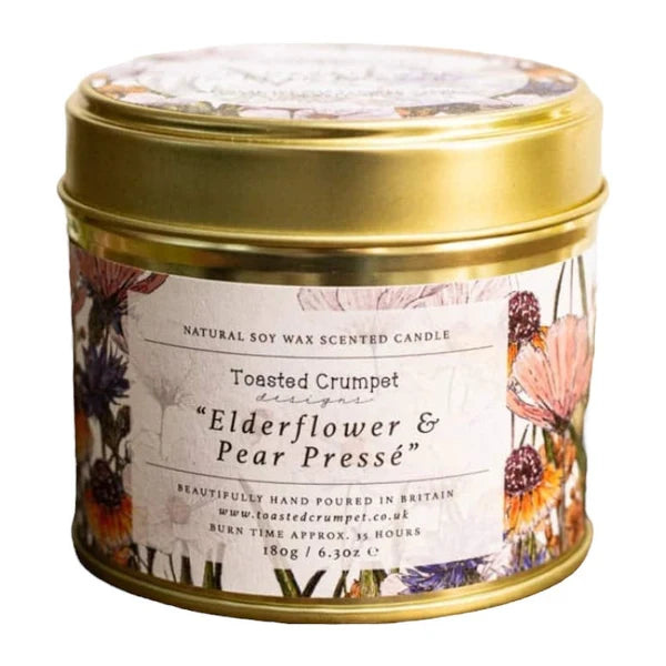 A round metal tin candle with a gold lid and a floral label reading 'Toasted Crumpet design Elderflower & Pear Pressé'.