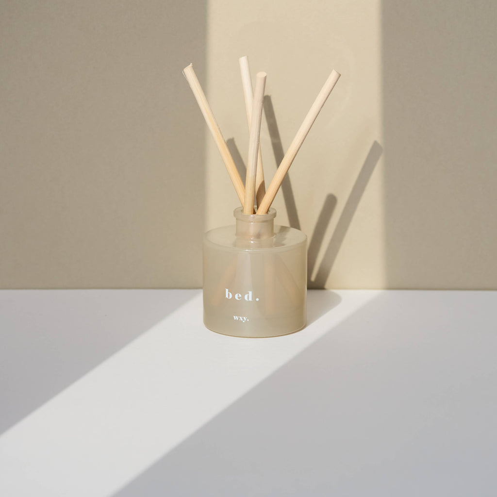 Reed diffuser with wooden sticks in a beige container on a white surface with a beige background