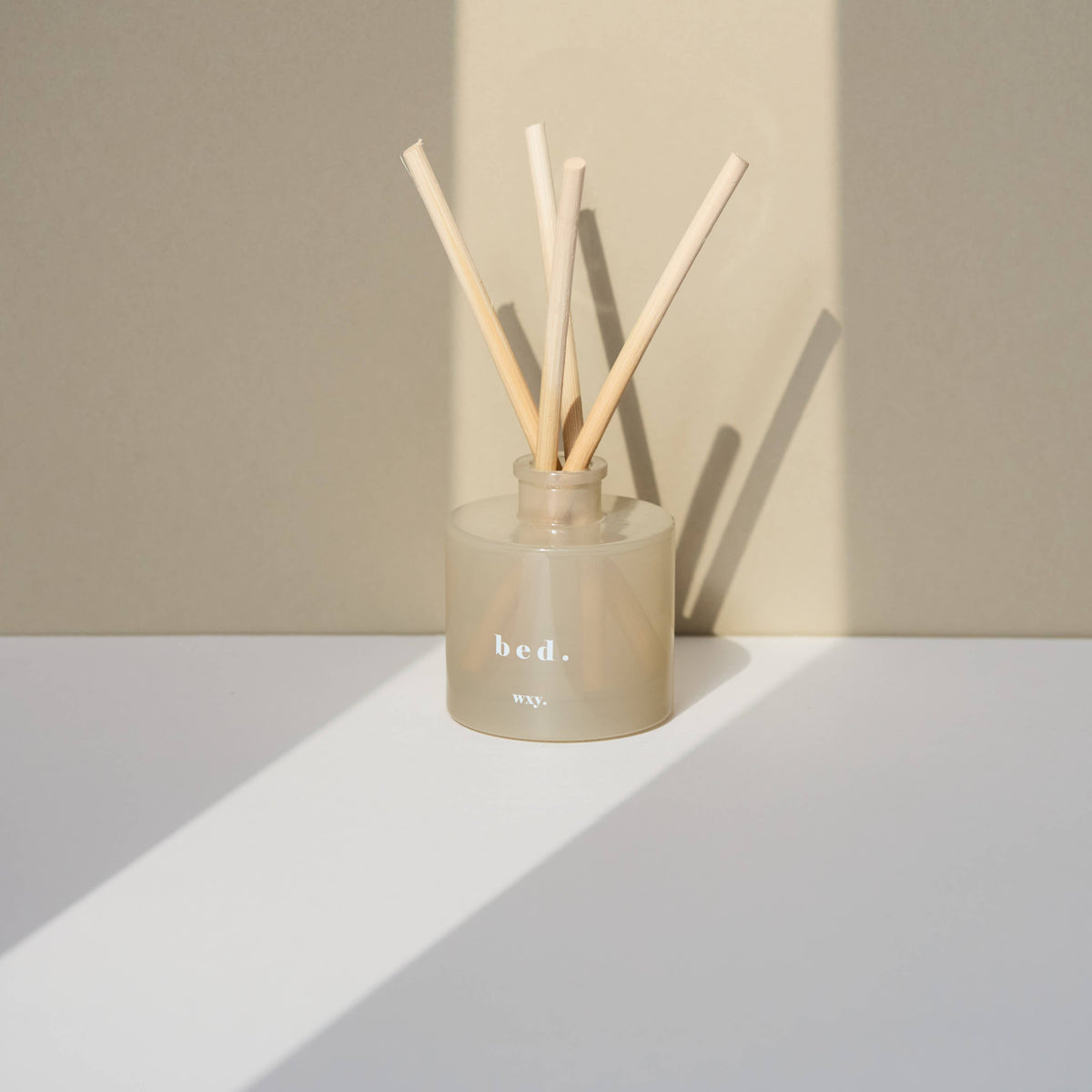 Reed diffuser with wooden sticks in a beige container on a white surface with a beige background