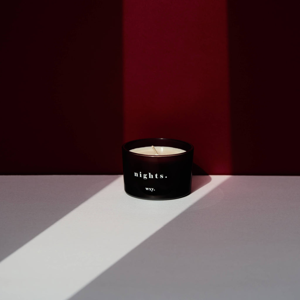 Candle in a black container labeled 'nights.' by 'wyy.' on a white surface with a red background