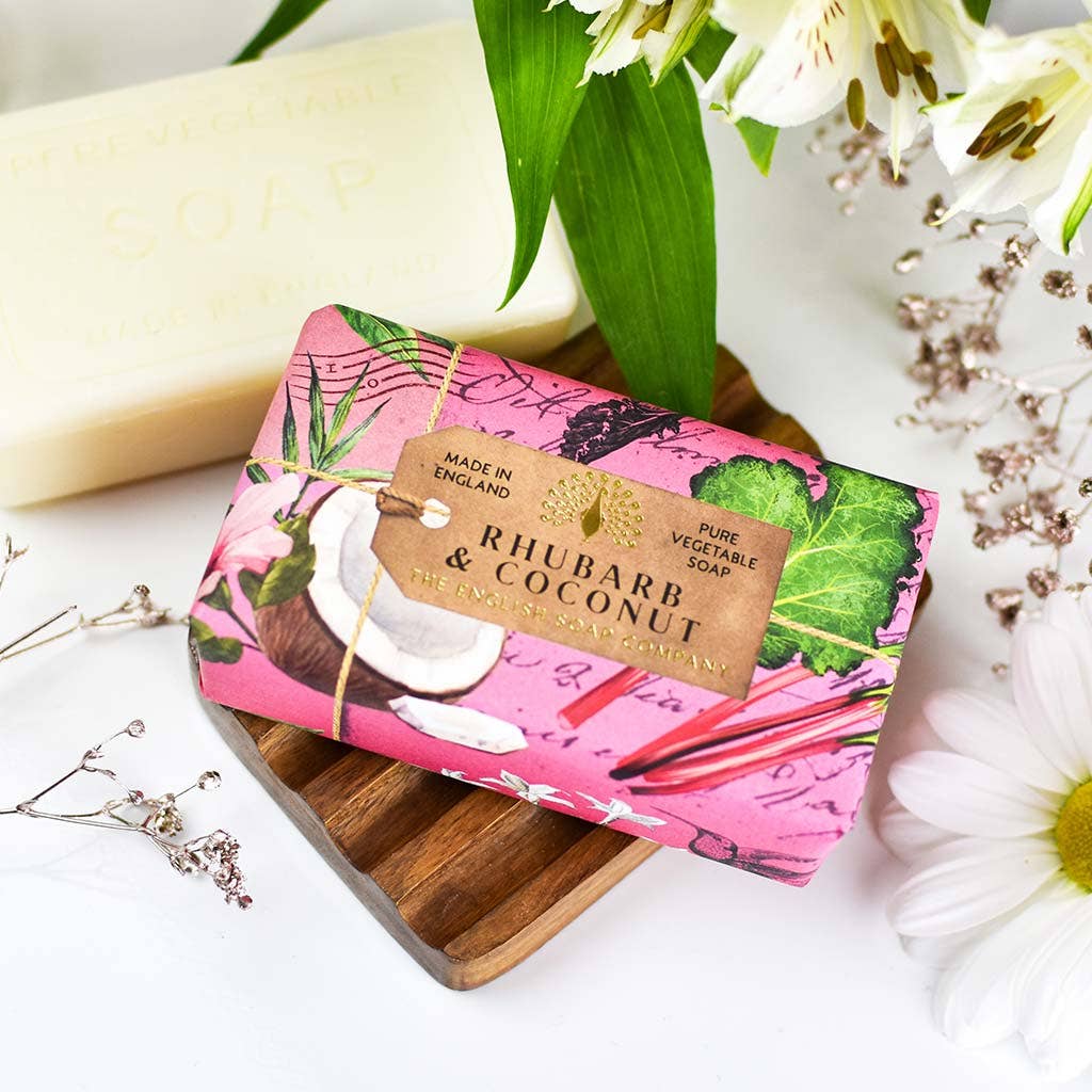 Bar of soap with pink packaging featuring rhubarb and coconut design, tied with string on a wooden board.