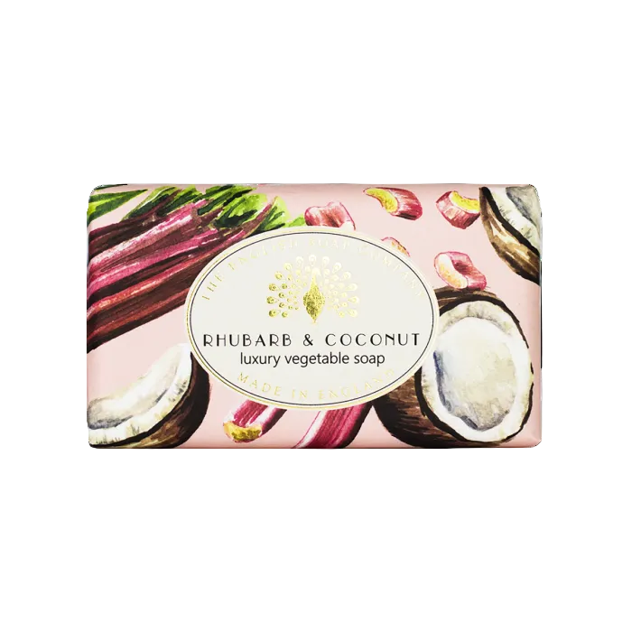 A rectangular bar of soap wrapped in pink paper featuring an illustration of rhubarb stalks, coconut halves, and a central oval label that reads 'RHUBARB & COCONUT luxury vegetable soap'. - The Fig House