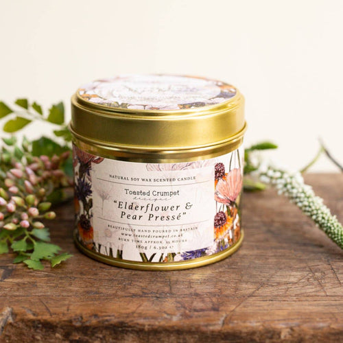 Scented candle in a decorative tin with floral design on a wooden surface