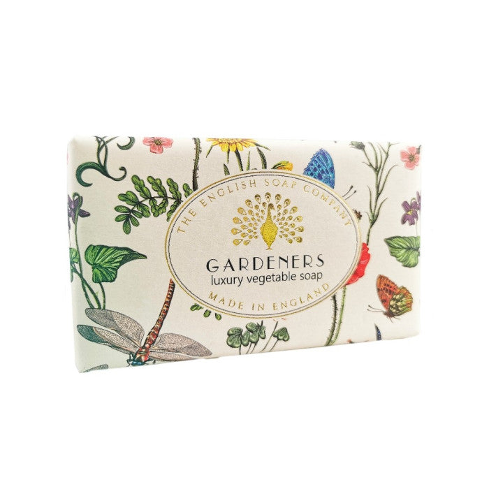 A rectangular bar of Gardeners luxury vegetable soap by The English Soap Company, wrapped in an off-white paper featuring colorful botanical illustrations of flowers, leaves, butterflies, and a dragonfly, with a gold circular logo in the center. - The Fig House