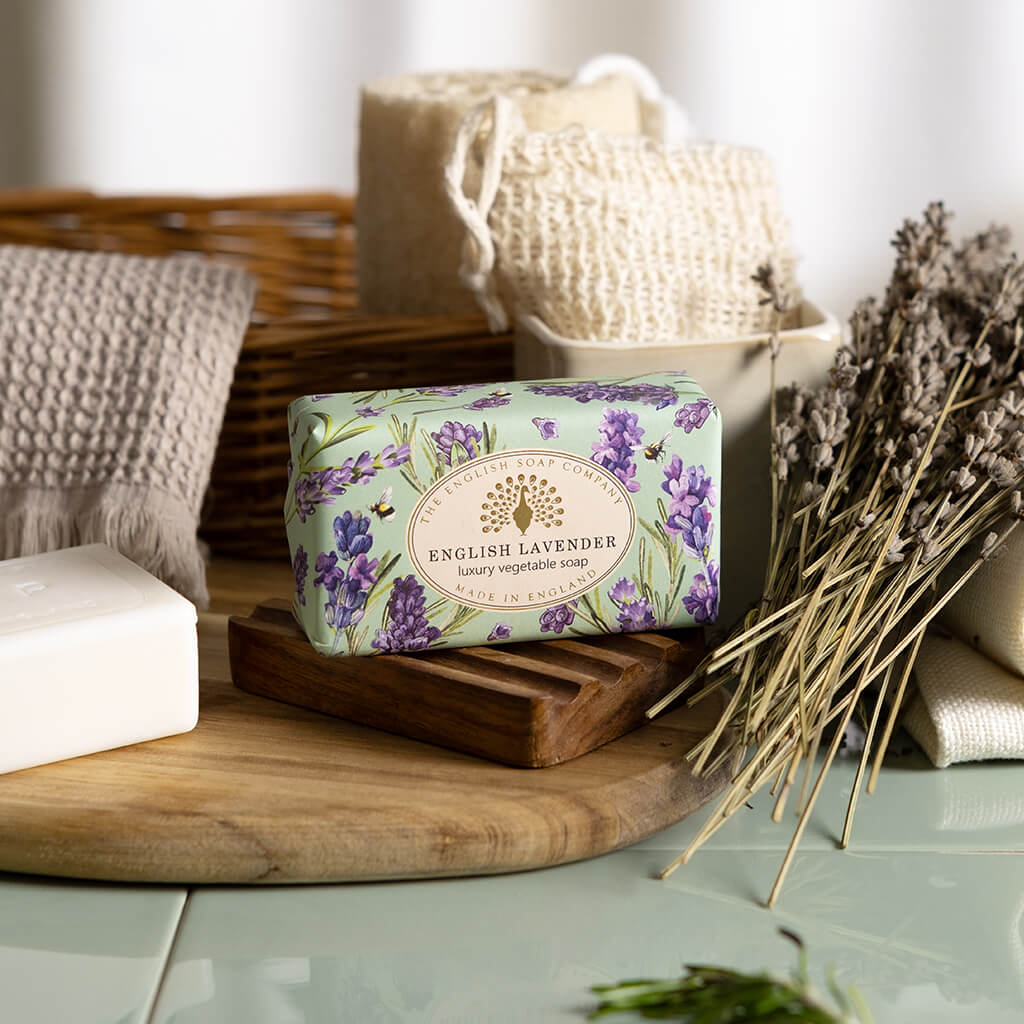 Bar of English Lavender soap on a wooden tray with lavender flowers and a woven basket in the background.