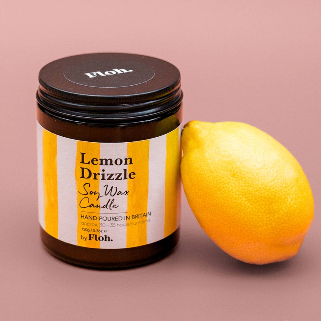 Jar of 'Lemon Drizzle' soy wax candle by Floh with a lemon on a pink background