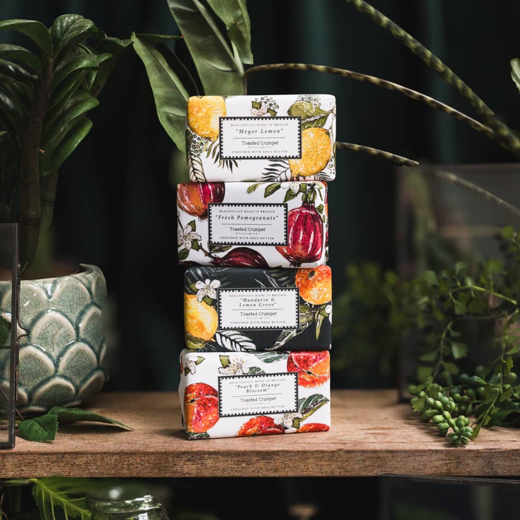 Stack of decorative boxes with fruit designs on a wooden surface with plants in the background