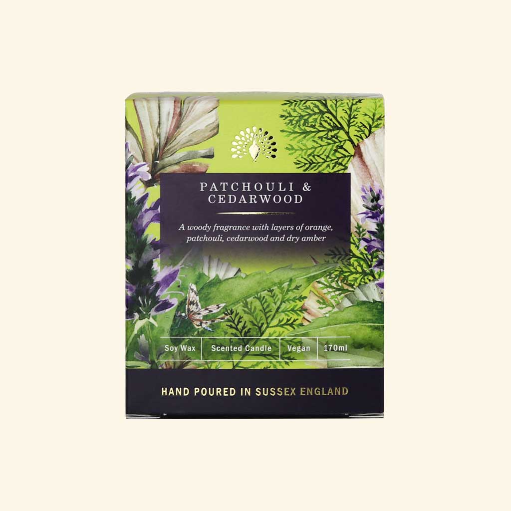 Patchouli & Cedarwood soy wax candle packaging, featuring a botanical illustration of green leaves and purple patchouli flowers on a light beige background. - The Fig House