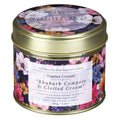 A cylindrical tin candle with a gold metal lid and a colorful floral label, shown on a plain white background. The label reads 'Toasted Crumpet' and 'Rhubarb Compote & Clotted Cream'.