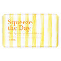 A rectangular bar of soap with rounded corners, featuring a watercolor-style yellow and white vertical stripe pattern. The front is printed with the text 'Squeeze the Day' in orange, along with smaller scent and brand text reading 'by Floh.